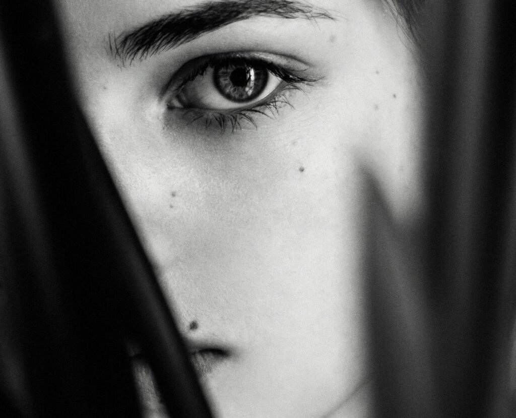 Intriguing black and white portrait of a woman partially obscured by foliage.